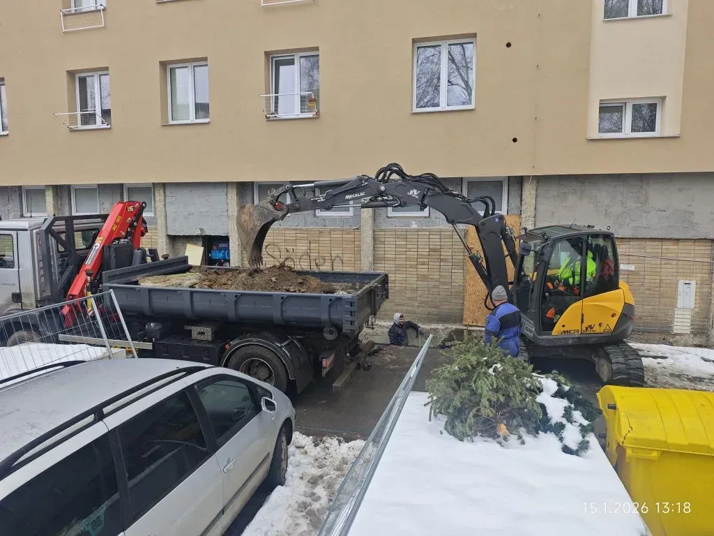 Rypadlo nakládá stavební suť na sklápěč u bytového domu