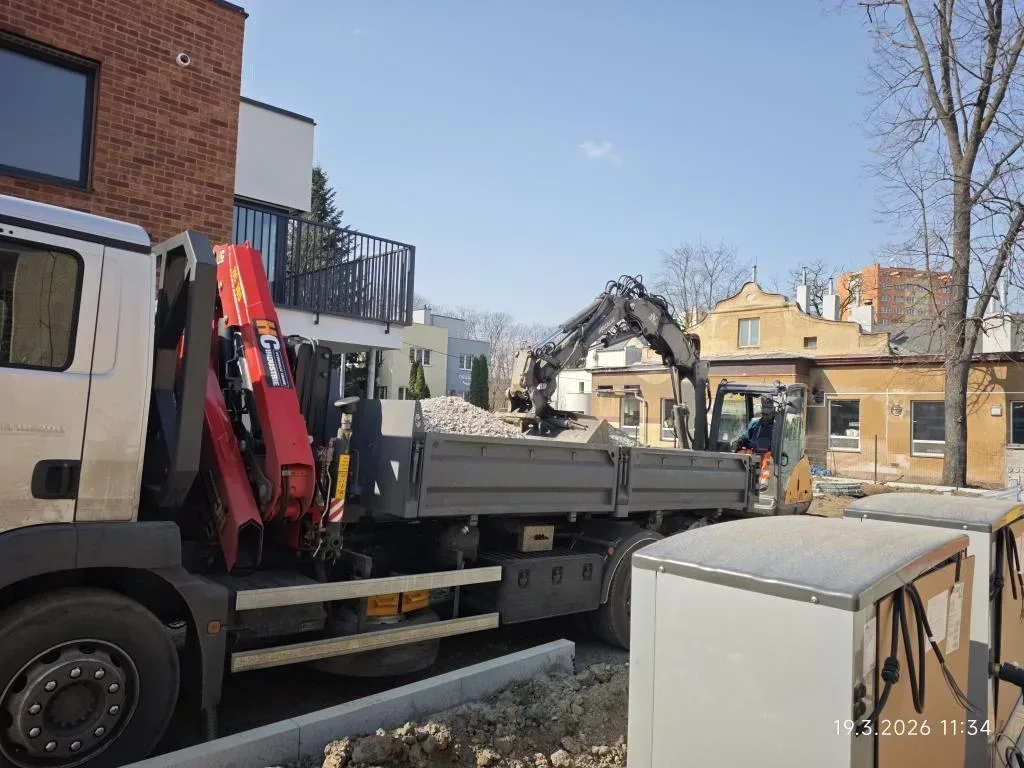 Nákladní vůz s hydraulickou rukou a rypadlo na stavbě u bytového domu