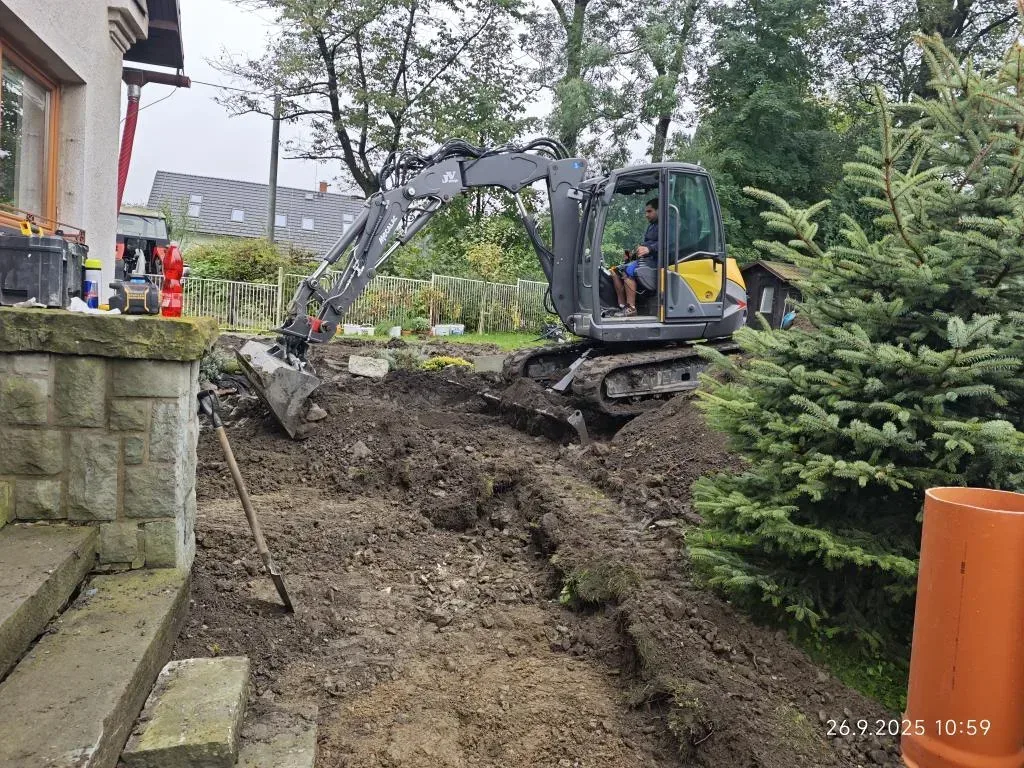 Rypadlo hloubí rýhu pro přípojku podél rodinného domu